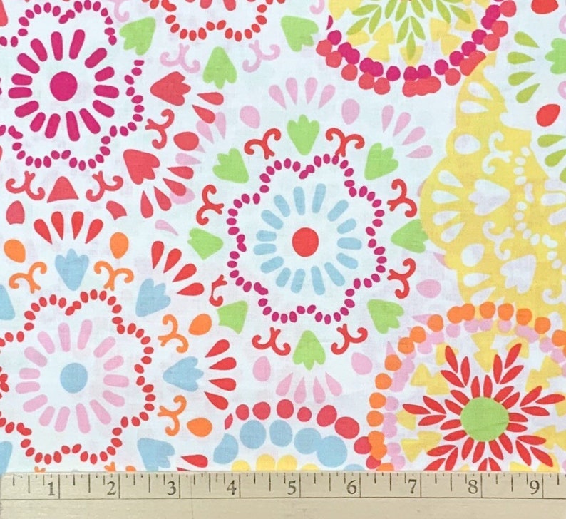 May include: White fabric with a colorful floral pattern. The design features circular motifs in shades of pink, red, orange, yellow, green, and blue. The fabric is decorated with stylized flower and leaf shapes.