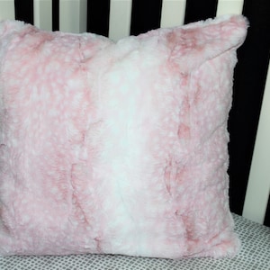 May include: A soft pink and white faux fur throw pillow. The pillow has a subtle ombre effect with a white center and pink edges.