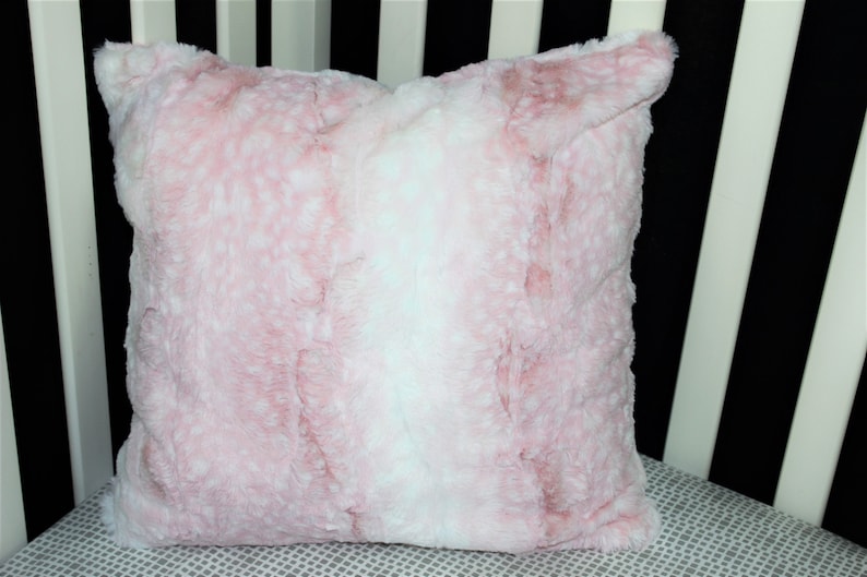 May include: A soft pink and white faux fur throw pillow. The pillow has a subtle ombre effect with a white center and pink edges.
