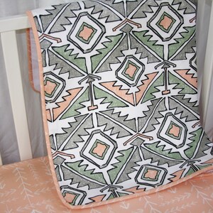 May include: A white crib sheet with a peach and green geometric pattern. The sheet has a peach border and is made of soft, breathable fabric.