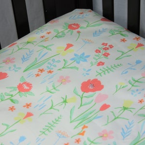 May include: A white crib sheet with a floral pattern featuring pink, blue, and yellow flowers on a white background.