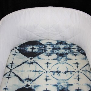 May include: A white crib with a blue and white patterned fitted sheet. The crib is made of wood and has a white fabric lining.