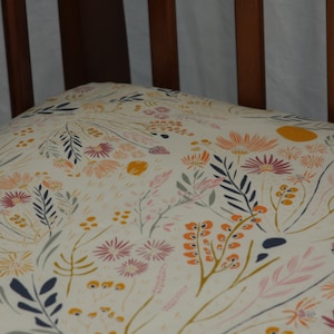 May include: A white fitted crib sheet with a floral pattern featuring pink, orange, and yellow flowers and navy blue leaves.