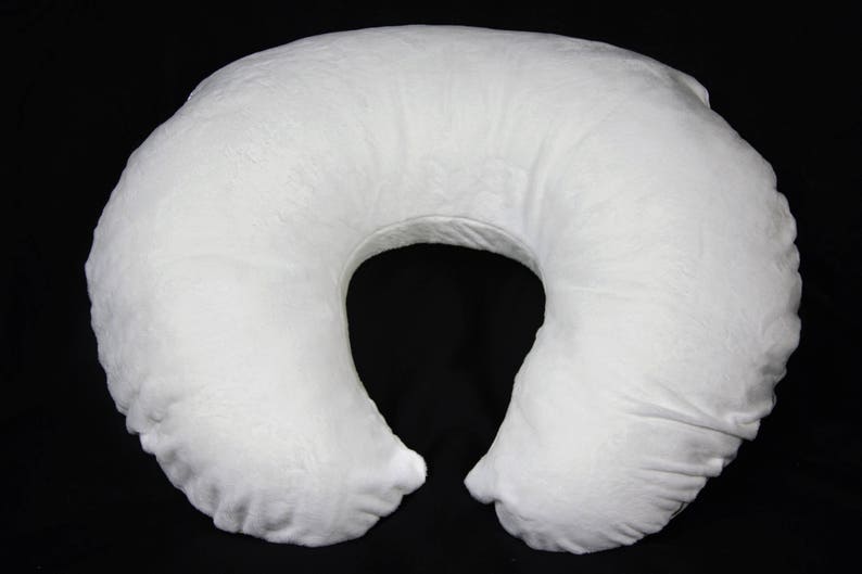 May include: A white, U-shaped pregnancy pillow with a soft, plush fabric cover. The pillow is designed to provide support and comfort during pregnancy and breastfeeding.