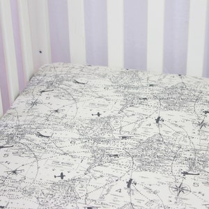 May include: A white crib sheet with a black and white airplane print. The sheet features a map of the world with flight paths and compass roses. The text "The World" appears on the sheet.