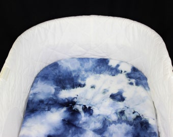 May include: A white baby bassinet with a blue and white tie-dye patterned fitted sheet.
