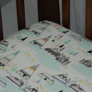 May include: A white crib sheet with a pattern of green, orange, and gray mountains and trees. The sheet is made of soft, breathable fabric and is perfect for a baby's crib.