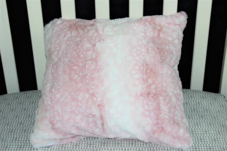 May include: A pink and white faux fur throw pillow with a soft, fluffy texture.