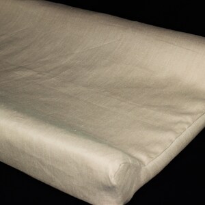 May include: A beige changing pad made of soft fabric with a slightly textured surface.