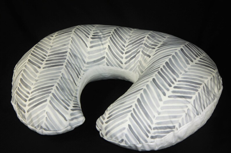 May include: A white and gray patterned nursing pillow shaped like a crescent moon. The pillow has a chevron pattern with gray lines on a white background.