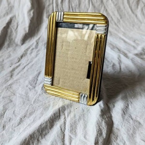 May include: A gold picture frame with a silver trim. The frame is empty and ready for a photo.