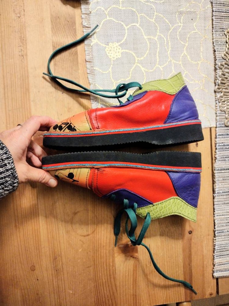 Puede incluir: Un par de zapatos de cuero multicolores con cordones verdes. Los zapatos tienen una suela de goma negra y est&aacute;n decorados con un dise&ntilde;o colorido.