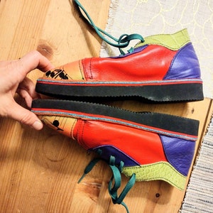 Puede incluir: Un par de zapatos de cuero rojo, verde, morado y amarillo con cordones. Los zapatos tienen una suela de goma negra y un dise&ntilde;o &uacute;nico de patchwork.