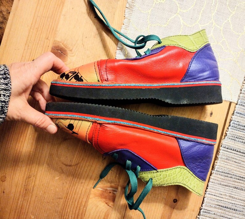 Puede incluir: Un par de zapatos de cuero rojo, verde, morado y amarillo con cordones. Los zapatos tienen una suela de goma negra y un dise&ntilde;o &uacute;nico de patchwork.