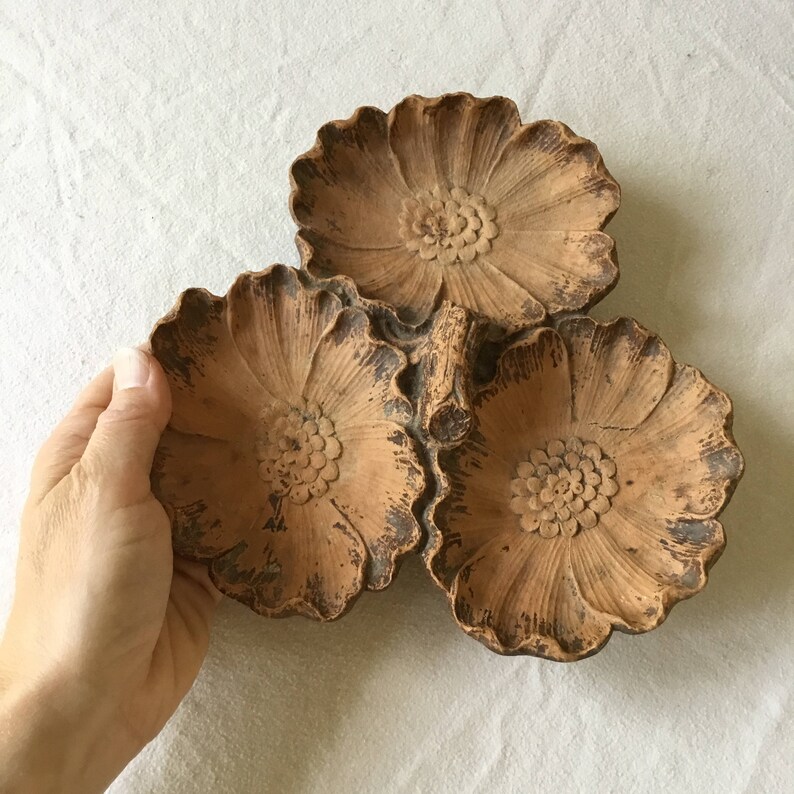 K&ouml;nnte beinhalten: Drei terracottafarbene, blumenf&ouml;rmige Schalen mit einem erh&ouml;hten Zentrum und gewellten R&auml;ndern. Die Schalen sind in der Mitte durch einen erh&ouml;hten Stiel verbunden.