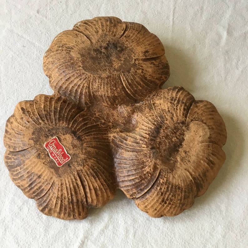 K&ouml;nnte beinhalten: Eine dreiteilige Servierplatte aus Holz mit brauner Oberfl&auml;che. Die Platte ist in Form von drei sich &uuml;berlappenden Blumen geformt. Die Platte tr&auml;gt ein Etikett mit der Aufschrift "Ornawood Made in U.S.A."