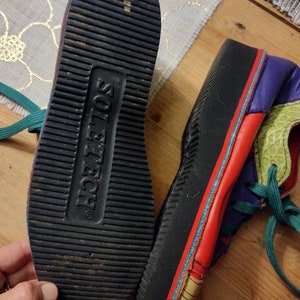 Puede incluir: Un par de zapatillas multicolores con suela negra. Las zapatillas tienen una parte superior de cuero rojo, verde, azul y morado. La suela est&aacute; marcada con el texto "Sole Tech".