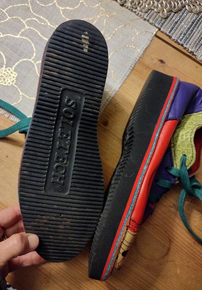 Puede incluir: Un par de zapatillas multicolores con suela negra. Las zapatillas tienen una parte superior de cuero rojo, verde, azul y morado. La suela est&aacute; marcada con el texto "Sole Tech".