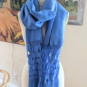 May include: A blue woven shawl with a fringe border. The fringe is made of a delicate, openwork pattern.