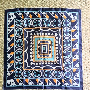 May include: A navy blue bandana with a geometric pattern in orange, white, and blue. The pattern features circles, squares, and teardrop shapes.