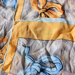 Puede incluir: Una tela con estampado amarillo y azul con un diseño repetitivo de lazos. La tela está doblada y muestra el patrón en ambos lados.