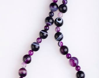 May include: A purple and black agate gemstone necklace with a silver clasp and a silver bead with a decorative design. The necklace is made of round beads and is approximately 20 inches long.