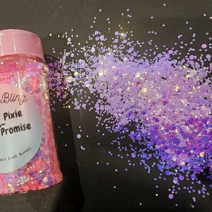 May include: A clear plastic jar with a pink lid filled with pink and iridescent glitter. The label reads "Fairy Bling Pixie Promise". A pile of purple and iridescent glitter is scattered to the right of the jar.