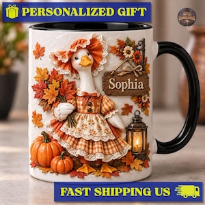 Peut inclure: Un mug en céramique blanche avec une anse et un intérieur noirs, orné d'une illustration en relief d'une oie portant un bonnet orange et une robe à carreaux. L'oie tient des feuilles d'automne près de deux citrouilles, une lanterne et un panneau Sophia.