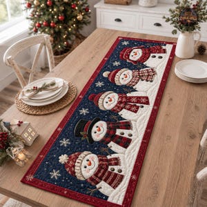 Peut inclure: Un chemin de table matelassé rectangulaire sur fond bleu marine, orné d'un motif répétitif de cinq bonhommes de neige portant des écharpes et des bonnets à carreaux rouges et noirs, avec des flocons de neige brodés et une bordure rouge.