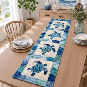 May include: A rectangular quilted table runner featuring four square panels, each displaying a blue sea turtle graphic. The runner is designed with a patchwork border of various blue and teal fabric shades, creating a cohesive aquatic theme.