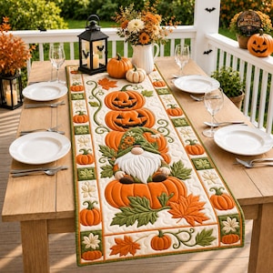Puede incluir: Un camino de mesa acolchado que presenta un gnomo central sentado sobre una calabaza, rodeado de calabazas naranjas bordadas y hojas de otoño verdes. El camino tiene un fondo blanco con un borde decorativo de pequeñas calabazas y hojas.