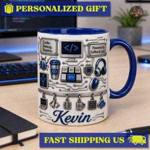 Könnte beinhalten: Ein weißer Keramikbecher mit dunkelblauem Innenraum und Henkel, verziert mit einer 3D-Grafik aus Computerhardware, Leiterplattenmustern sowie dem Text Code. Debug. Deploy., Powered by Coffee & Logic und dem Namen Kevin in blauer Schrift.