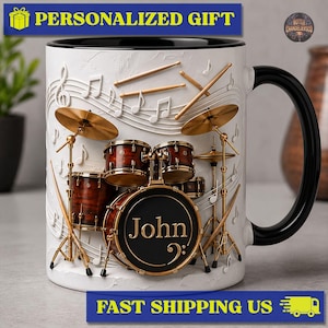 Peut inclure: Un mug en céramique blanc avec une anse et un intérieur noirs, présentant un motif en relief 3D d'une batterie avec des cymbales dorées et des fûts marron. La grosse caisse porte le nom John et une clé de fa. Des notes de musique ornent la surface.