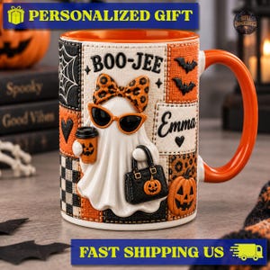 May include: A ceramic mug featuring a white ghost character wearing orange leopard print sunglasses and a matching bow. The ghost holds a coffee cup and a black handbag. The mug has a patchwork design with pumpkins, bats, and the text BOO-JEE and Emma.