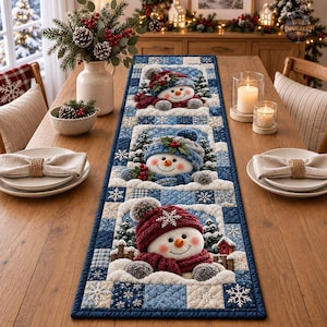 May include: A rectangular quilted table runner featuring a blue and white patchwork pattern with snowflake motifs. Three distinct panels display snowmen wearing textured hats and scarves, surrounded by small pine trees and snowy accents.