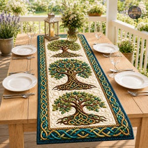 May include: A rectangular quilted table runner featuring three embroidered tree motifs with intricate brown trunks and green leaves. The runner has a cream-colored center and a decorative border with a blue and gold Celtic knot pattern.