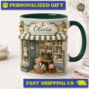 Può includere: Una tazza in ceramica con un'illustrazione dettagliata di una boutique di cucito con tenda a righe verdi, una macchina da cucire, rocchetti di filo e un cesto di stoffa. L'insegna sopra la porta recita Olivia Sewing Boutique.