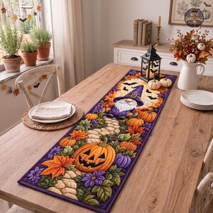 Puede incluir: Un camino de mesa rectangular de tela con temática de Halloween que presenta un gnomo con sombrero morado, rodeado de calabazas naranjas, flores moradas, hojas verdes y murciélagos negros sobre un fondo de camino de piedra claro.