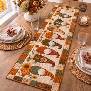 May include: A rectangular quilted table runner featuring a repeating pattern of gnomes wearing patterned hats, interspersed with sunflowers and pumpkins in shades of orange, green, and cream, finished with a checkered border in autumn colours.