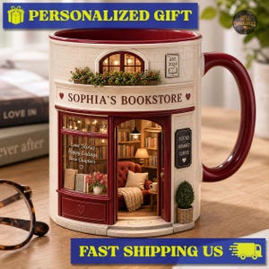May include: A ceramic mug shaped like a bookstore storefront with a cream-colored brick exterior, a deep red door, and a handle. The facade features the text "SOPHIA'S BOOKSTORE" and a window display showing a miniature interior with a red chair.