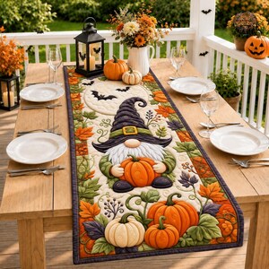 Könnte beinhalten: Ein gesteppter Tischläufer mit einem zentralen Wichtel mit hohem violettem Hut, umgeben von orangefarbenen und weißen Kürbissen sowie Herbstblättern. Das Design zeigt einen Vollmond mit schwarzen Fledermaussilhouetten auf hellem Grund.