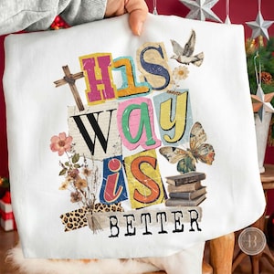 May include: White sweatshirt with a colorful graphic design. The design features the words "THIS WAY IS BETTER" in a collage style, along with a cross, flowers, a butterfly, a dove, and books.