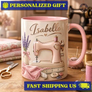 May include: A cream-coloured ceramic mug with a pink interior and handle, featuring a pink sewing machine illustration, a lavender bouquet, a measuring tape, and buttons. The name Isabelle is printed in gold script above the sewing machine.