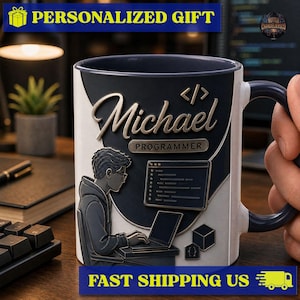 May include: A ceramic mug with a dark blue and white design featuring a graphic of a person sitting at a laptop. The text Michael and Programmer are printed on the front along with a code snippet icon and a set of brackets. The mug has a dark blue handle.