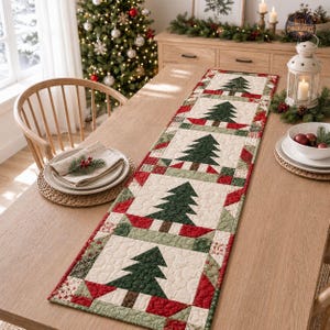 May include: A quilted table runner featuring a repeating pattern of dark green Christmas trees on a cream background, bordered by red and green patchwork fabric. The runner is laid flat on a wooden table with a folded napkin and a white lantern.