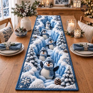 Puede incluir: Un camino de mesa rectangular con un paisaje invernal de colinas nevadas en azul y blanco, árboles de hoja perenne y cinco pingüinos con bufandas y gorros azules. El diseño incluye patrones de copos de nieve blancos.