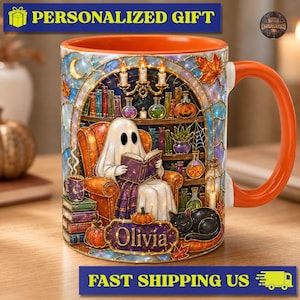 May include: A ceramic mug with an orange interior and handle, featuring a colorful illustration of a ghost reading a book in an armchair, surrounded by bookshelves, potions, a black cat, and pumpkins, with the name Olivia printed on a plaque.