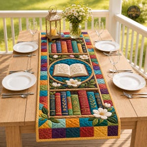 Puede incluir: Un camino de mesa acolchado rectangular que presenta un motivo circular central de un libro abierto rodeado de flores blancas, flanqueado por filas de lomos de libros verticales coloridos, bordeado por un patrón de parches de cuadrados multicolores.