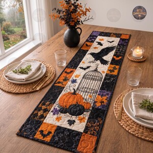 May include: A rectangular quilted table runner featuring a Halloween theme with a black crow, a birdcage, pumpkins, and bats. The fabric pattern includes orange, black, and purple autumn leaves. The runner is centered on a wooden table with place settings.