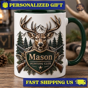 Puede incluir: Una taza de cerámica blanca con interior y asa de color verde oscuro. El frente presenta una ilustración detallada de una cabeza de ciervo, pinos y montañas. Debajo del ciervo hay un escudo verde con el texto Mason HUNTING CLUB.